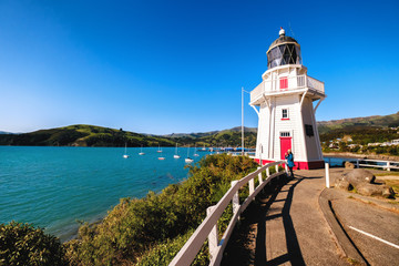 A beautiful lighthouse locate in Akaroa, New Zealand. This is a perfect holiday destination. It is popular among tourists, backpackers, and locals. One can enjoy clear blue sky, ocean, and shops. - obrazy, fototapety, plakaty