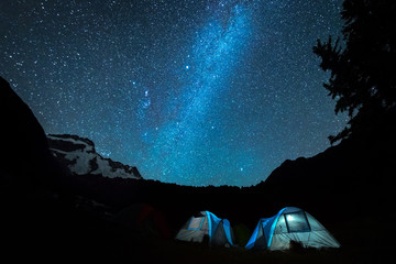 Outdoor travel activity tents at camp site with night sky, milky way galaxy and stars.