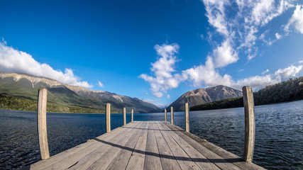 A calming background of a dock in New Zealand. The lake is very beautiful, clear and refreshing. There are mountain, blue sky and white cloud. This image is suitable for adding text or words.