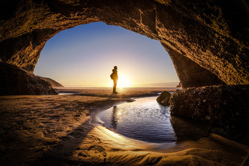 People explores a cave during sunrise at Wharariki Beach New Zealand - obrazy, fototapety, plakaty