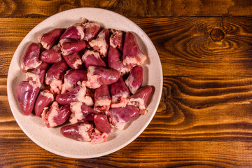 Ceramic plate with raw chicken hearts on wooden table. Top view
