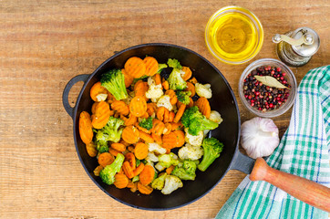 Stewed vegetables in oil on old pan, wooden table