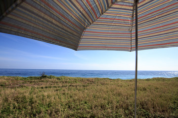 A colorful umbrella by the coast. It was a sunny beautiful day and it is perfect for a walk along the coast. The view is beautiful. There are high cliff. This image is suitable for background use.