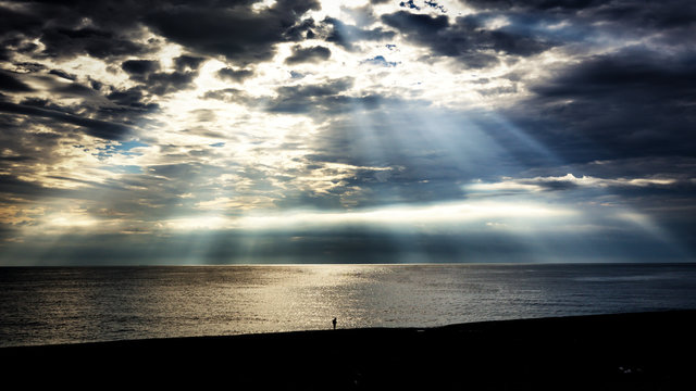 An underexposed image (intentional) to bring out the details of the magnificent light rays. There is a person in the middle. One can feel the relative size of a human and the ocean.