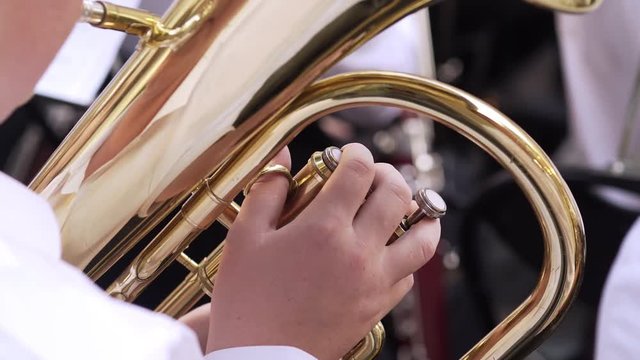 Outdoor concert young man in white shirt playing trumpet in orchestra, close-up shot part of musical instrument and fingers pressing on bottons.Leipzig, Germany
