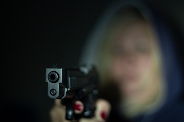 A woman holds a gun in her hand and points it at the camera . Focus on the front of the gun.