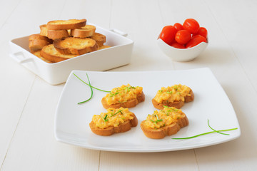 White plate with toasts and scrambled eggs, chive herbs and cherry tomatoes on white table background. Grilled bread with scrambled eggs and vegitable.