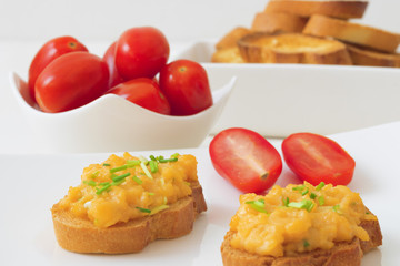 White plate with toasts and scrambled eggs, chive herbs and cherry tomatoes on white table background. Grilled bread with scrambled eggs and vegitable.