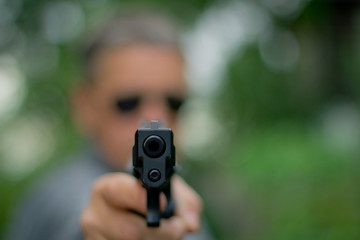 A man holds a gun in his hand and points it at the camera . Focus on the front of the gun.