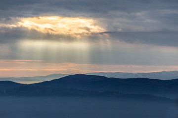 Fototapeta premium Sunray shines through clouds over the mountains and a sea of fog