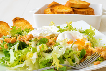 Classic French salad, great salad Lyonnaise. Dish with green leaves of lettuce, Dijon mustard sauce with pieces of fried bacon, grilled French bread, toasts and 2 poached eggs on the top.