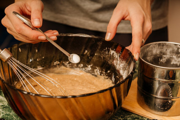 Obraz premium Crop housewife standing at table in kitchen and adding vanillin in bowl while preparing dough for cooking homemade pie