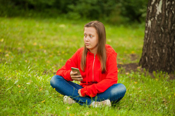 Fototapeta premium modern teenager girl sitting on the grass in the park with a smartphone in her hands