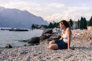 Beautiful young woman is sitting on the pebble beach and enjoying the view, vacation