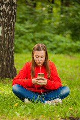 Fototapeta premium modern teenager girl sitting on the grass in the park with a smartphone in her hands