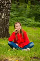 modern teenager girl sitting on the grass in the park with a smartphone in her hands