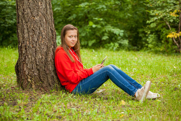 modern teenager girl sitting on the grass in the park with a smartphone in her hands