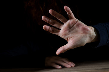 a woman is sitting in the dark and raises a hand defensively