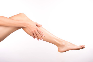 Fototapeta na wymiar Female hand with french manicure touches barefoot leg, isolated on white