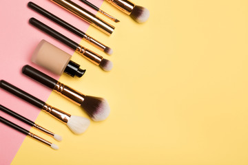 Professional makeup products with cosmetic beauty products, blushes, eye liner, eye lashes, brushes and tools on pink and yellow background