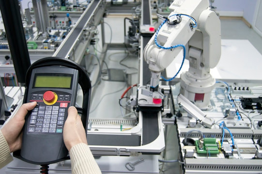 Man is holding teach panel (tablet) to control a robotic arm which is integrated on smart factory manufacturing line. industry 4.0 automation line which is equipped with sensors and robotic arm.