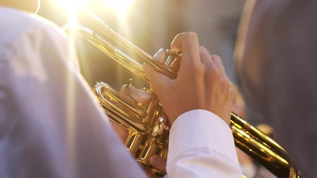 Open street concert classic music. Young man in white shirt playing trumpet in bright light. Close-up instrument in bright yellow light and hands pushing on battons.