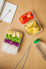 Healthy asian-style vegan bento box with rice, fried tofu, edamame beans and cherry tomatoes and pieces of pineapple with metal chopsticks on side, flatlay