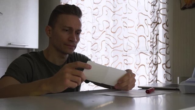 Man sitting at his desk, holding a sheet of paper in his hand and taking a two pieces of ticket. Close-up.
