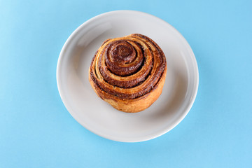 Cinnamon Danish Swirl-classic buttery danish pastry rolled with cinnamon and glazed with sugar on dish on blue paper background. Flat lay. Top view.