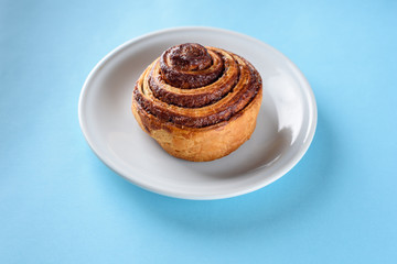 Cinnamon Danish Swirl-classic buttery danish pastry rolled with cinnamon and glazed with sugar on dish on blue paper background. Flat lay. Top view.