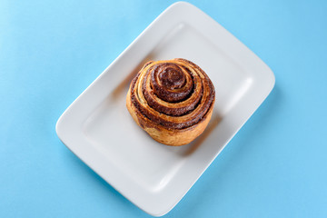 Cinnamon Danish Swirl-classic buttery danish pastry rolled with cinnamon and glazed with sugar on dish on blue paper background. Flat lay. Top view.