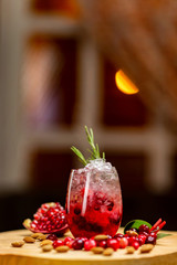 Vertical image of black currant cocktail with berries and frappe at decorated with pomegranate wooden table at evening window with moon and curtain background.