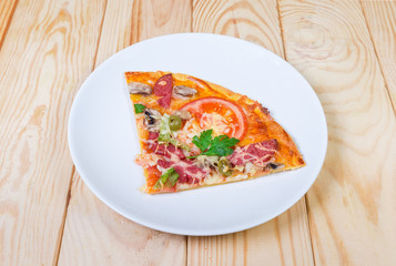 Pizza slice with salami on dish on rustic wooden table
