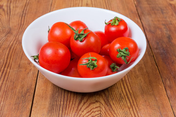 Red cherry tomatoes in white bowl on a rustic table