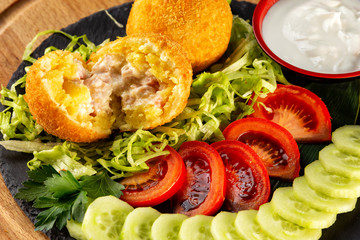 Two raprts of torn crispy golden round meat nuggets balls served with greens and sauce on wooden board background.