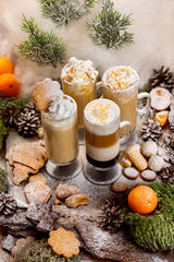 Vertical image of layered christmas coffee glasses set at decorated with moss, tangerines, cookies, sugar powder as a snow natural wooden board background.