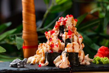 Plate of volcano sushi rolls with lava sauce at decorated with green palm tree and turtle object...
