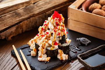Plate of volcano sushi rolls with lava sauce at decorated with wooden box and turtle object table bakground. © Mayatnikstudio