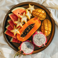 Flatlay of various exotic tropical fruits on a metal tray in bed, selective focus, square