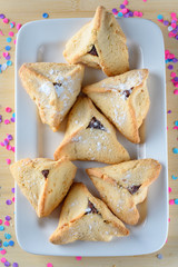 Hamantaschen cookies on white dish on wood table colorful confetti background. Purim holiday celebration.Top view.