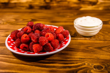 Ceramic plate with ripe raspberries and sour cream on wooden table