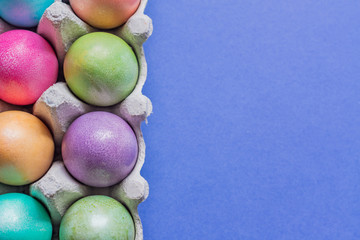 Multicolored easter eggs in a box . Top view on blue background.