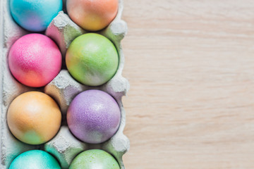 Multicolored easter eggs in a box. Top view on wooden background. Copy space for your text