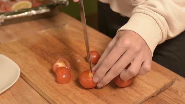 Closeup of the hands of a girl at the home kitchen on a wooden cutting board small cherry tomatoes. Home cooking