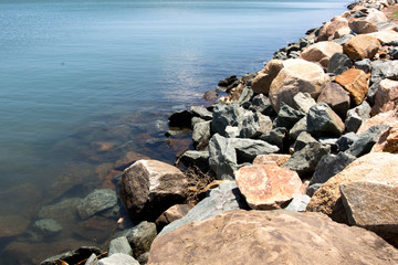 Fototapeta na wymiar Grey and brown rough rocks along the waters edge
