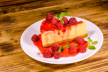 White plate with cheesecake New York, leaves of mint and raspberries on wooden table