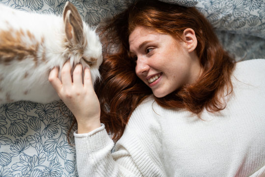 Smiling woman petting bunny on bed