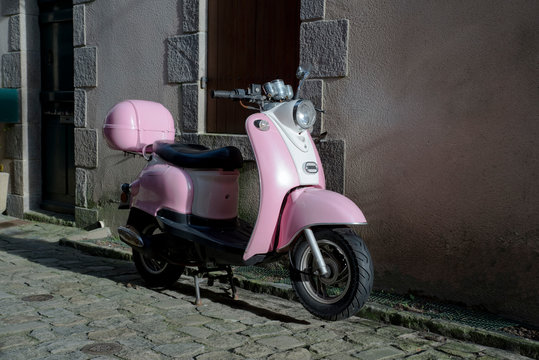 A pink scooter parked in a paved street in front of a wall