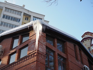 Icicles hang from roof of building. Danger for passers, threat of death and injury from icicles.