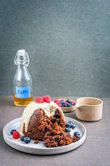 Traditional Australian plum pudding as closeup with fruits and vanilla rum sauce on a dessert plate with copy space